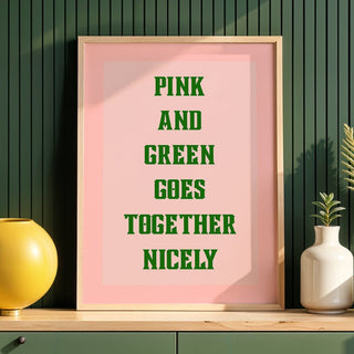 Framed poster with 'Pink and Green Goes Together Nicely' text on a pink background, placed on a wooden shelf against a green wall.