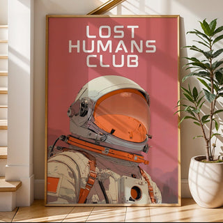 Framed poster titled 'Lost Humans Club' with an astronaut design on a pink background, placed on a staircase.