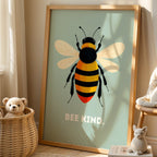 Framed artwork of a bee with 'BEE KIND' text in a room with a teddy bear and basket.