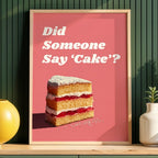 Framed poster with a cake illustration and text on a pink background, placed on a wooden shelf against a green wall.