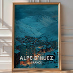 Illustrated 'Alpe d'Huez France' poster of a lit ski village nestled beneath snowy peaks at dusk